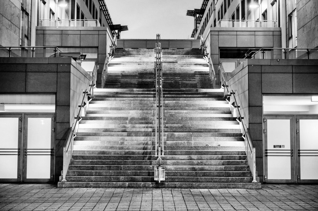 Schwarzweiß-Bild. Eine über mehrere Etagen aufsteigende, breite Treppe mit Abendlicher Beleuchtung. 